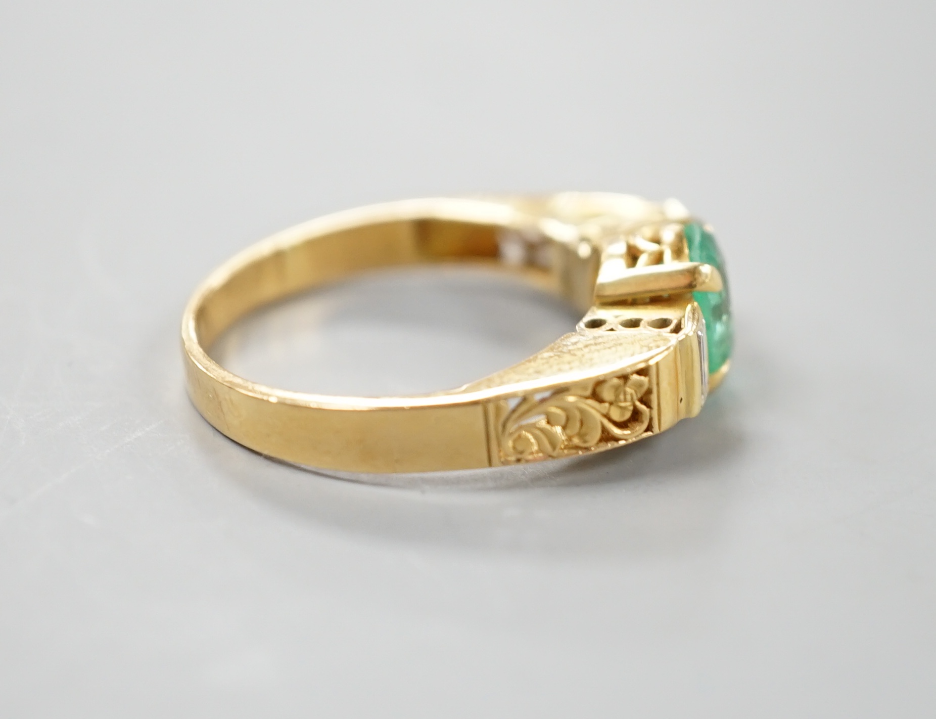 A modern yellow metal, round cut emerald and two stone baguette cut diamond set dress ring, with pierced shoulders, size Q/R, gross 5.5 grams.